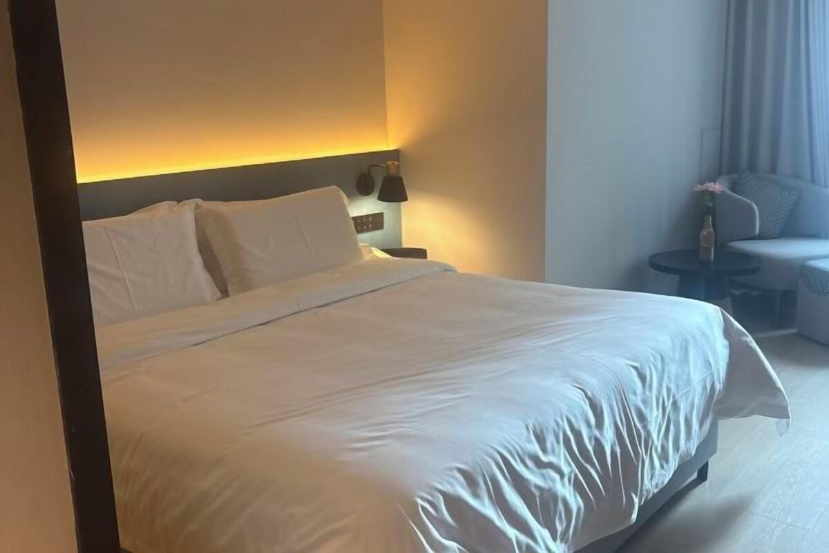 A hotel room with a large bed, a bedside table, a lamp, and a seating area with a chair and a small table.