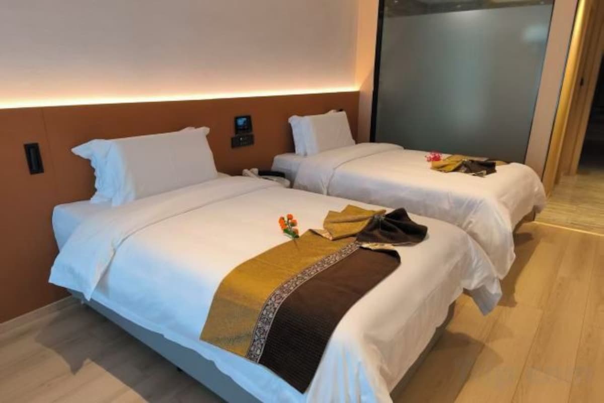 A hotel room with two beds, a nightstand, and a wall-mounted light.