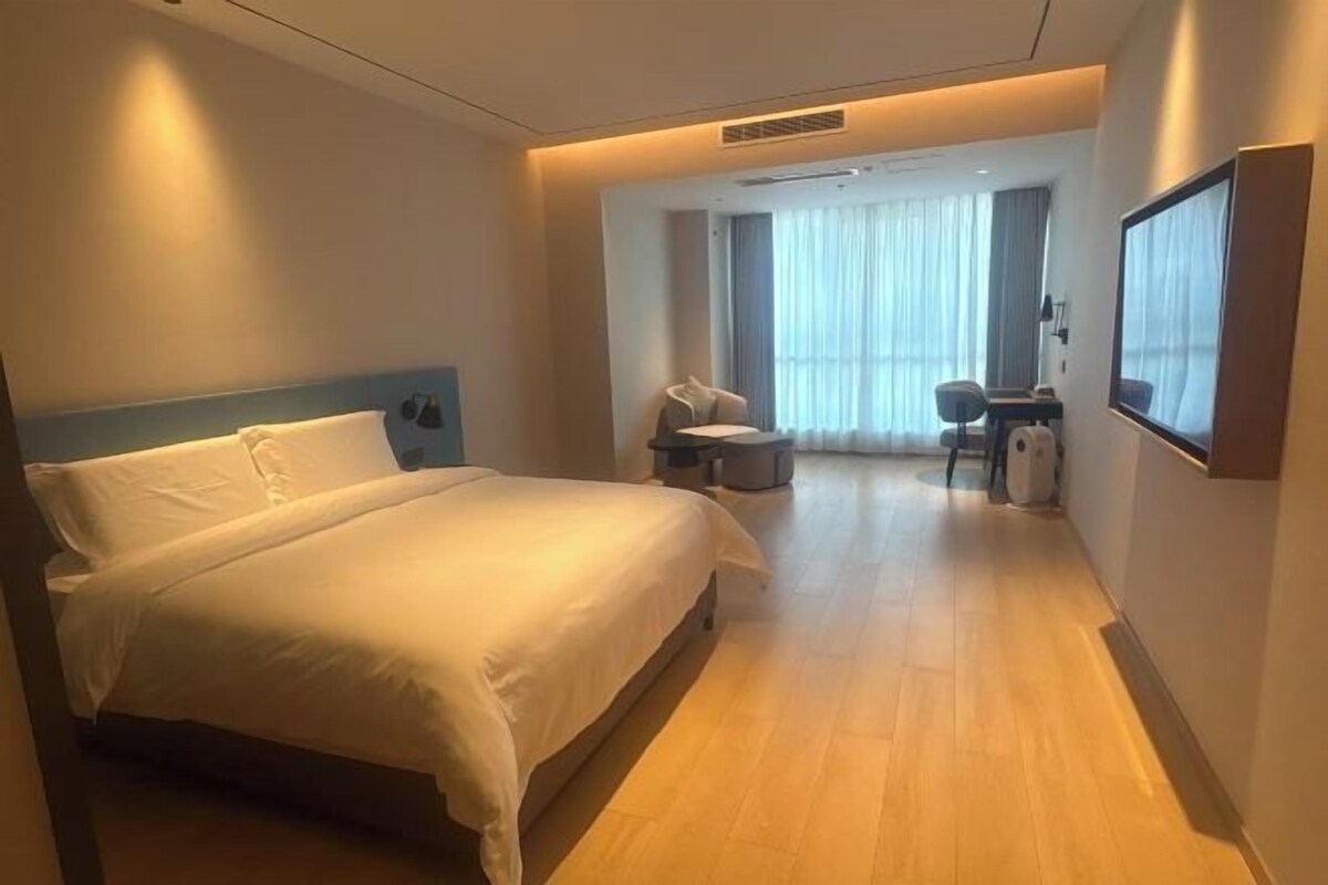 A hotel room with a bed, a desk, a chair, and a large window.