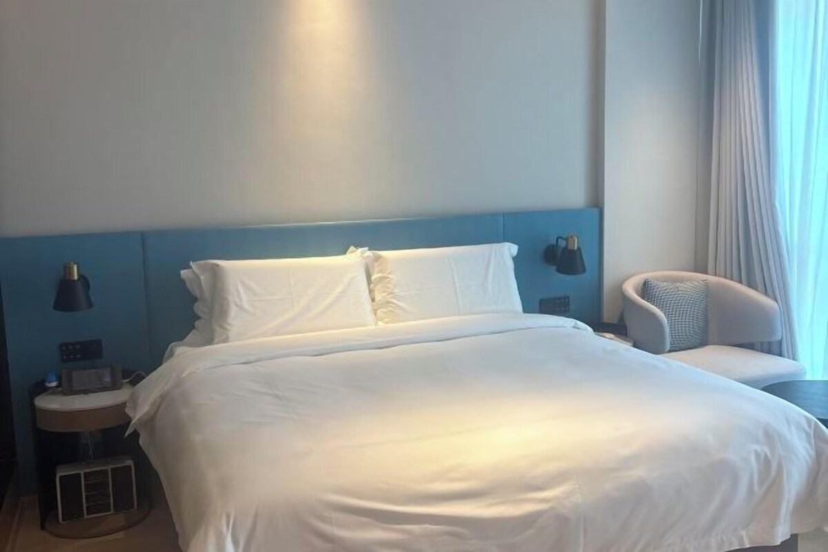 A hotel room with a large bed, bedside lamps, a chair, and a window with curtains.