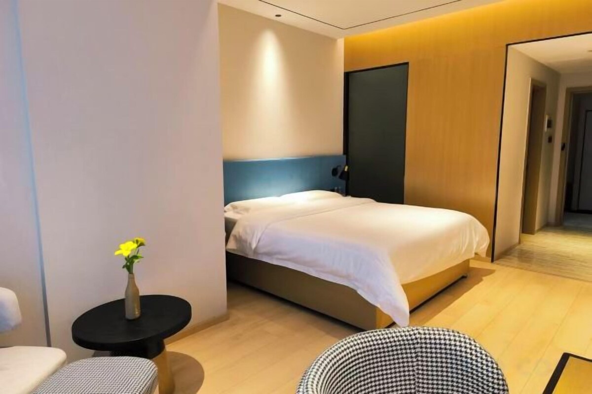 A modern hotel room with a bed, a small round table with a vase, and a chair.
