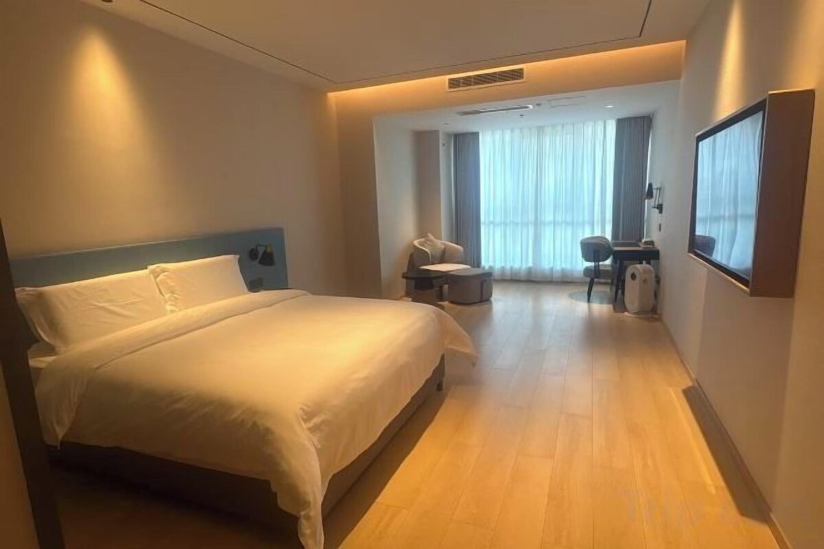 A hotel room with a bed, a desk, a chair, and a large window.