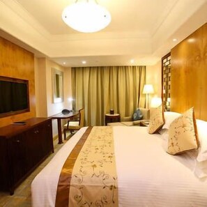 A hotel room with a large bed, a desk, a chair, a TV, and a lamp. - Harbour City Hotel (Jingmen)