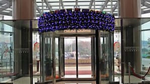 A revolving door with a blue floral decoration, glass panels, and a red rope barrier. - Harbour City Hotel (Jingmen)