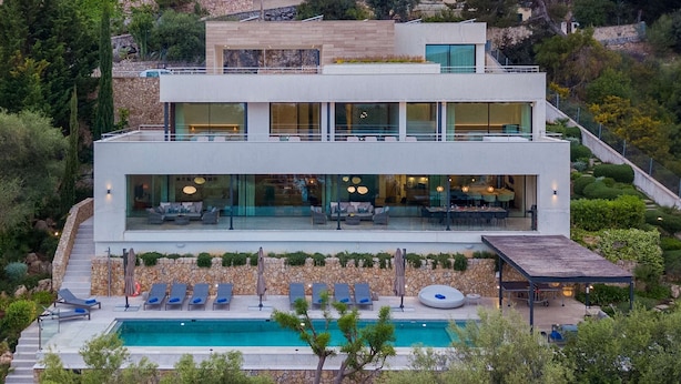 Ein modernes, zweistöckiges Haus mit Swimmingpool, Außenbereich zum Sitzen und einer Steinmauer.