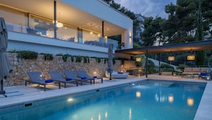 Ein moderner Poolbereich mit Liegestühlen, einer Steinmauer und einem überdachten Sitzbereich.