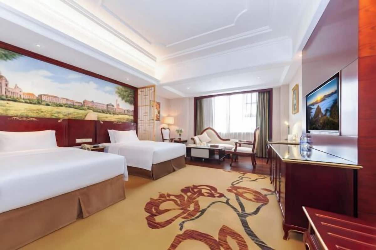 A hotel room with two beds, a desk, a TV, and a large window.