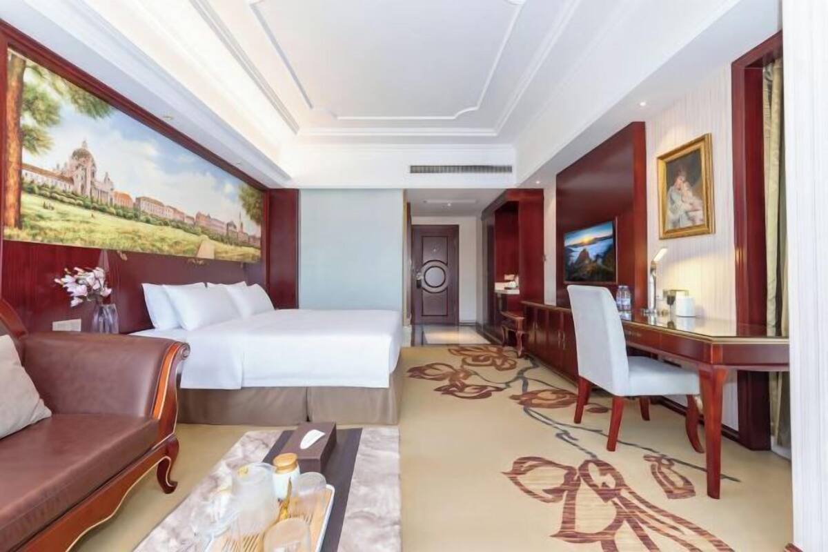 Quarto de hotel com cama, sofá, escrivaninha e televisão.