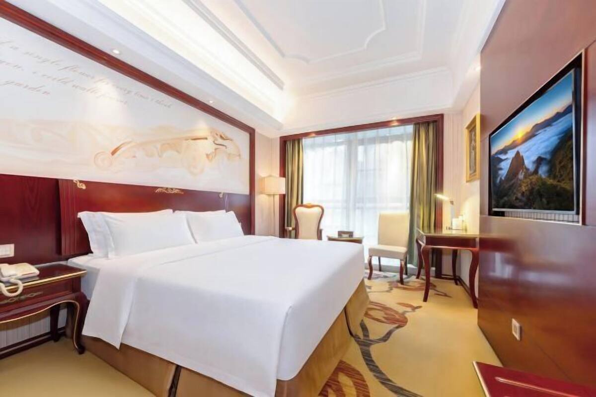 Quarto de hotel com cama grande, escrivaninha, cadeira, televisão e um mapa na parede.