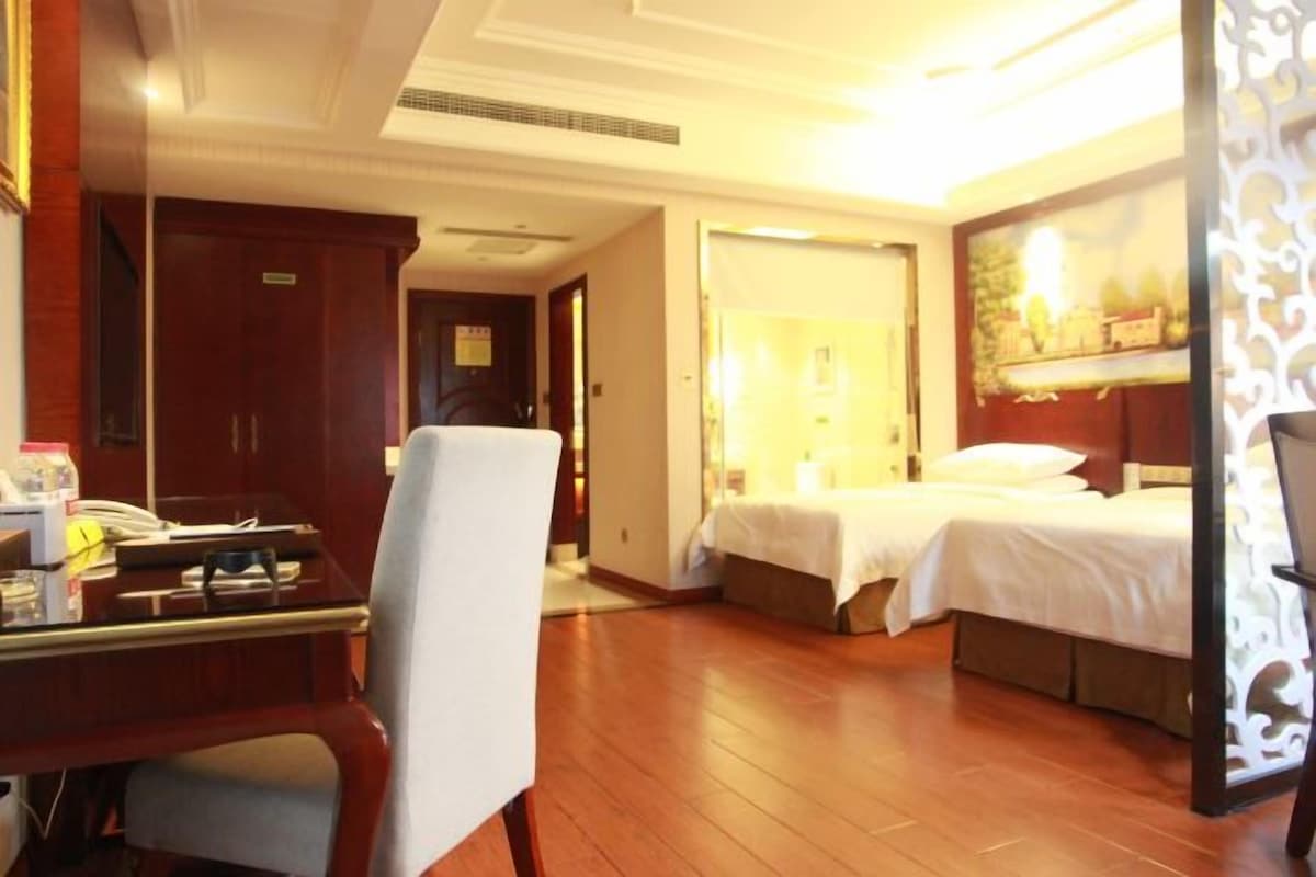 A hotel room with a desk, two beds, a chair, and a decorative wall.