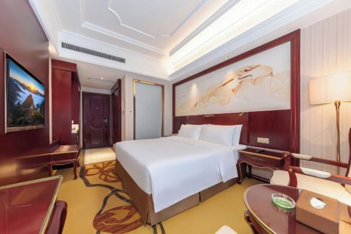 A hotel room with a large bed, a desk, a chair, a TV, and a painting on the wall.