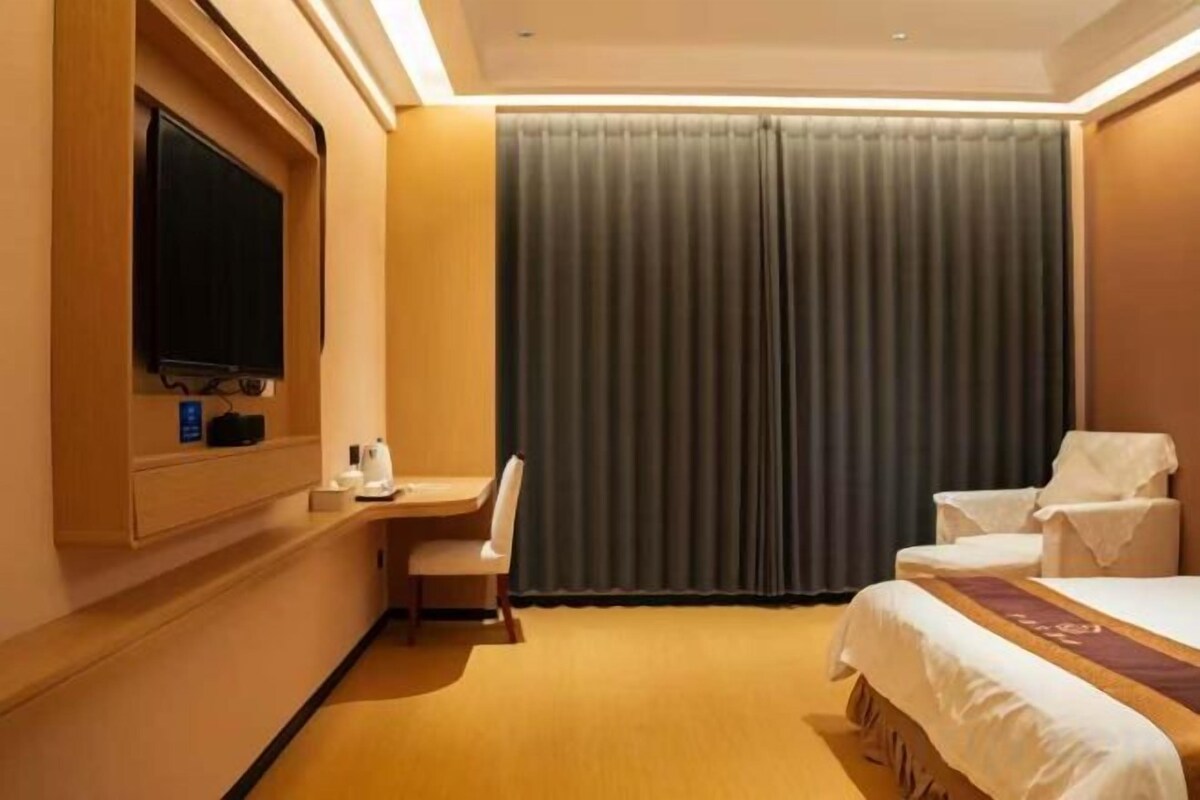 A hotel room with a bed, a desk, a chair, a television, and a large window with curtains.