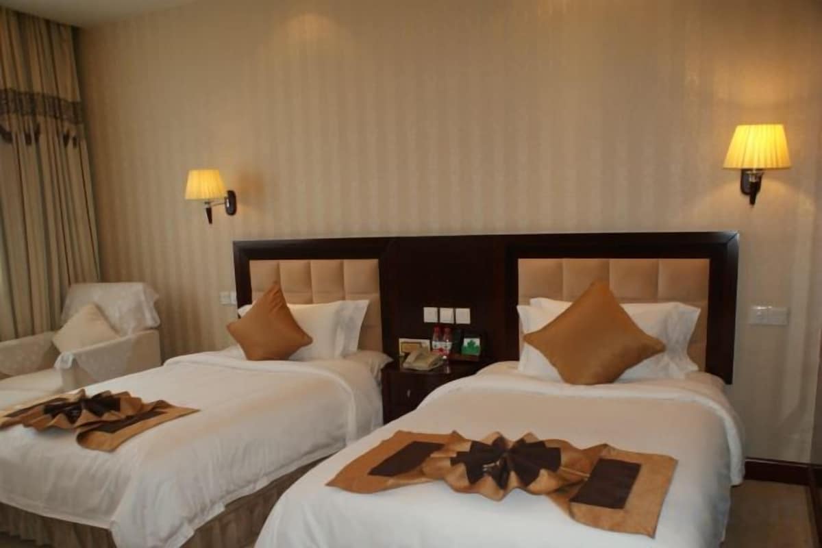 A hotel room with two beds, each with a pillow, bedside table, and a lamp.