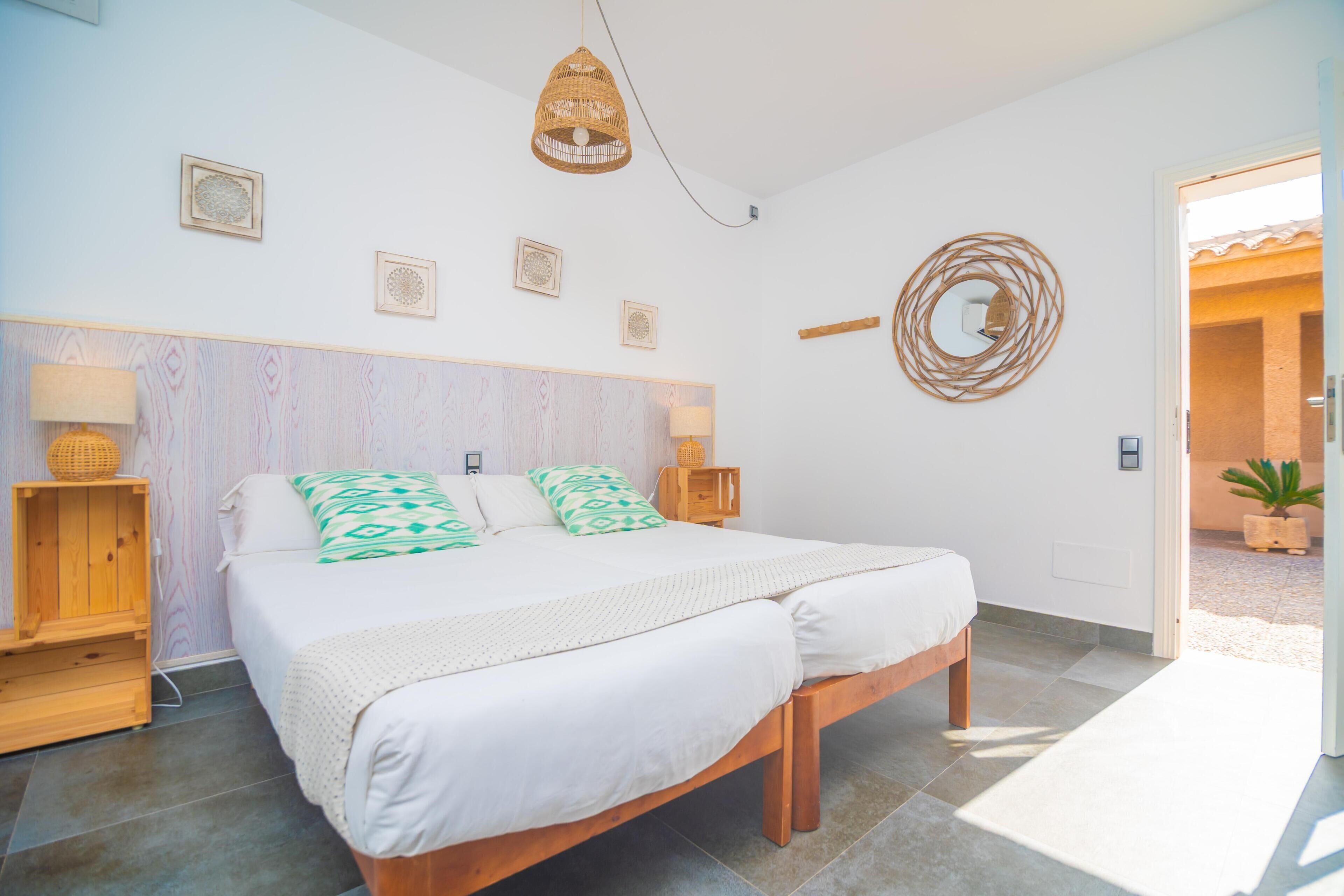 Un dormitorio con cama, lámparas de noche, cabecera de madera, adorno de pared tejido y una puerta que da al exterior.