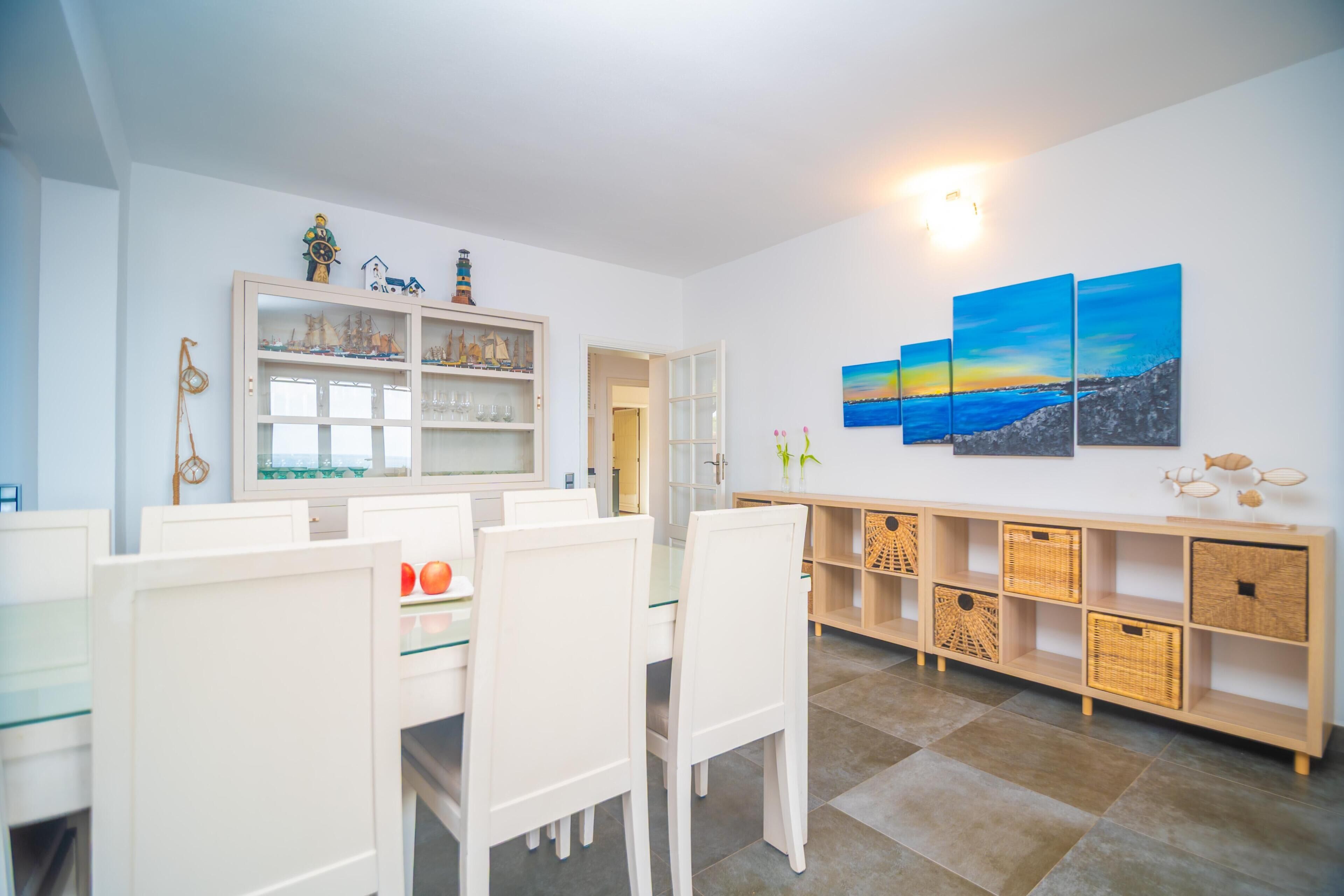 Ein Essbereich mit heller Möbel, einem Tisch mit Glasplatte und einer Wand mit einem Gemälde.
