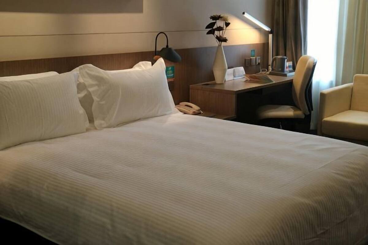 A hotel room with a large bed, a desk with a lamp, a chair, and a telephone.