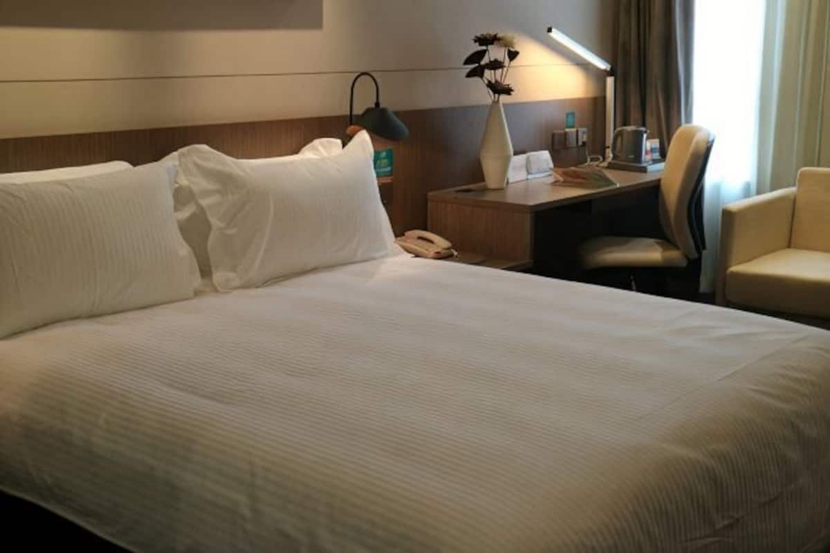 A hotel room with a large bed, a desk with a lamp, a chair, and a telephone.