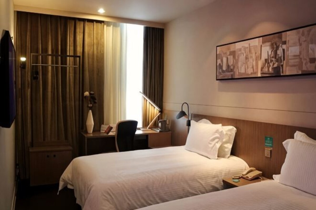 A hotel room with two beds, a desk, a chair, a TV, and a window with curtains.