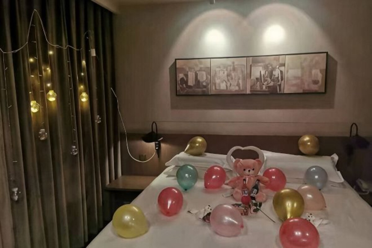 A room with a bed, balloons, string lights, and a wall-mounted picture.