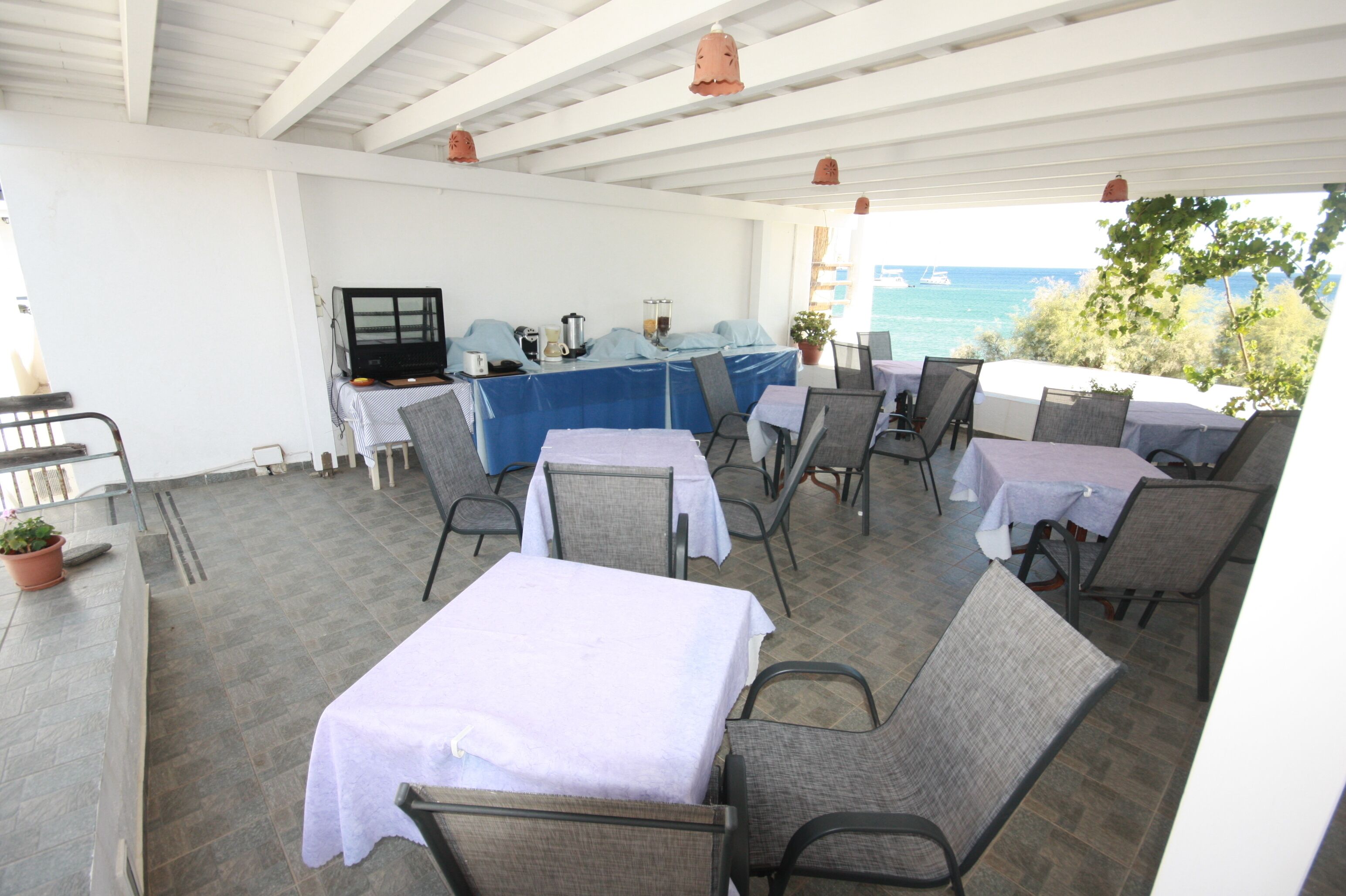 Un patio al aire libre con mesas y sillas, un televisor y vista al mar.