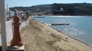 Una playa arenosa con vista clara al mar, un muelle de madera y edificios al fondo.