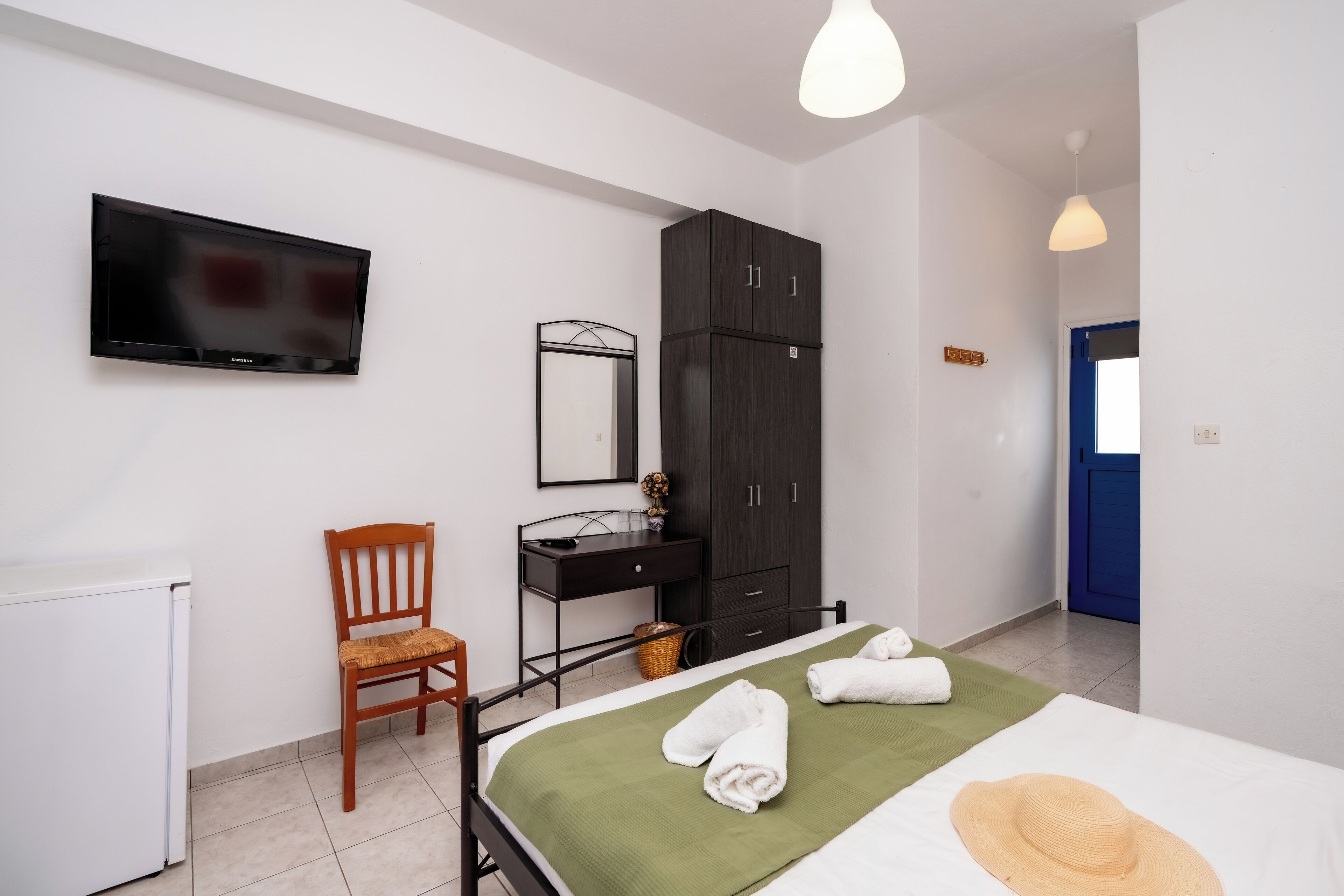 Un dormitorio con cama, escritorio, silla, armario, televisor y puerta.