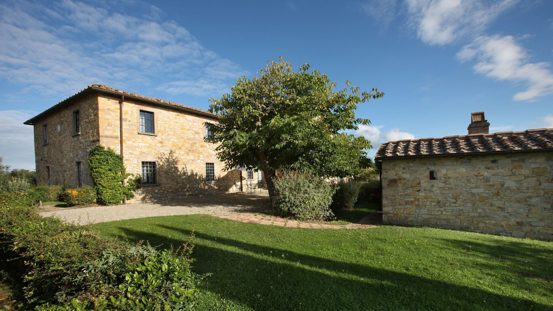 A stone building with a large tree in the front yard.