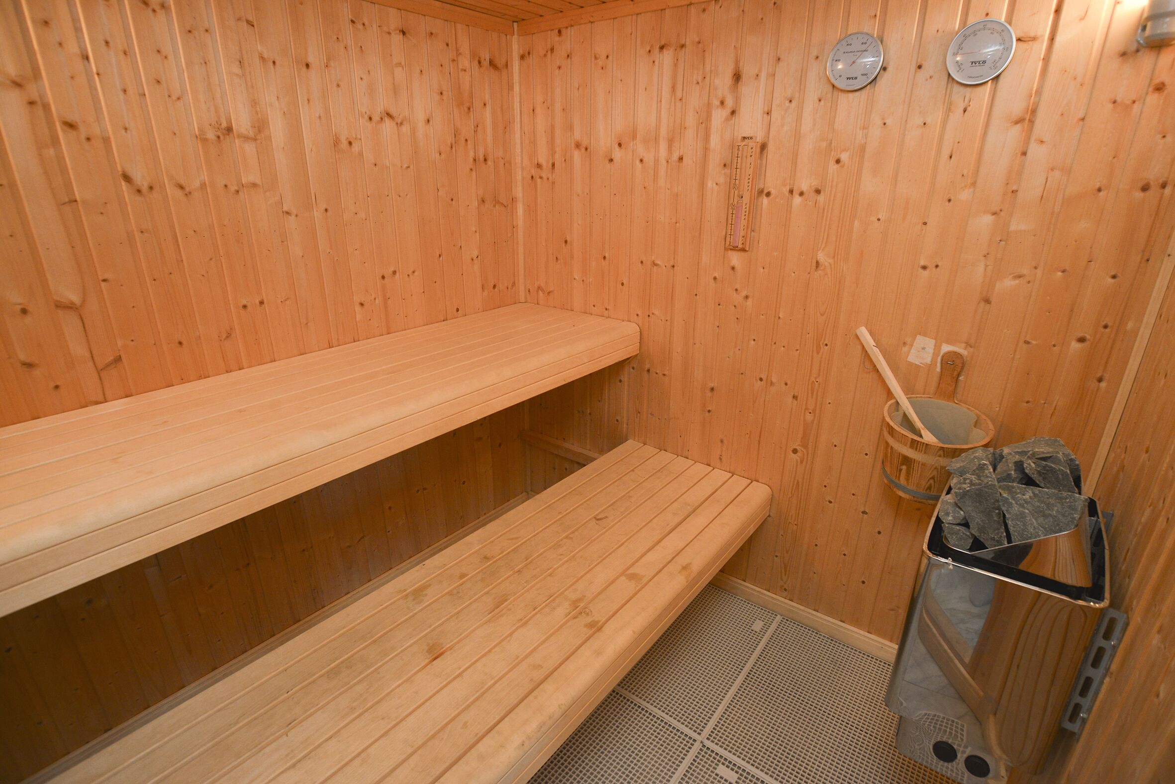 A wooden sauna with benches, a bucket, and a stone heater.