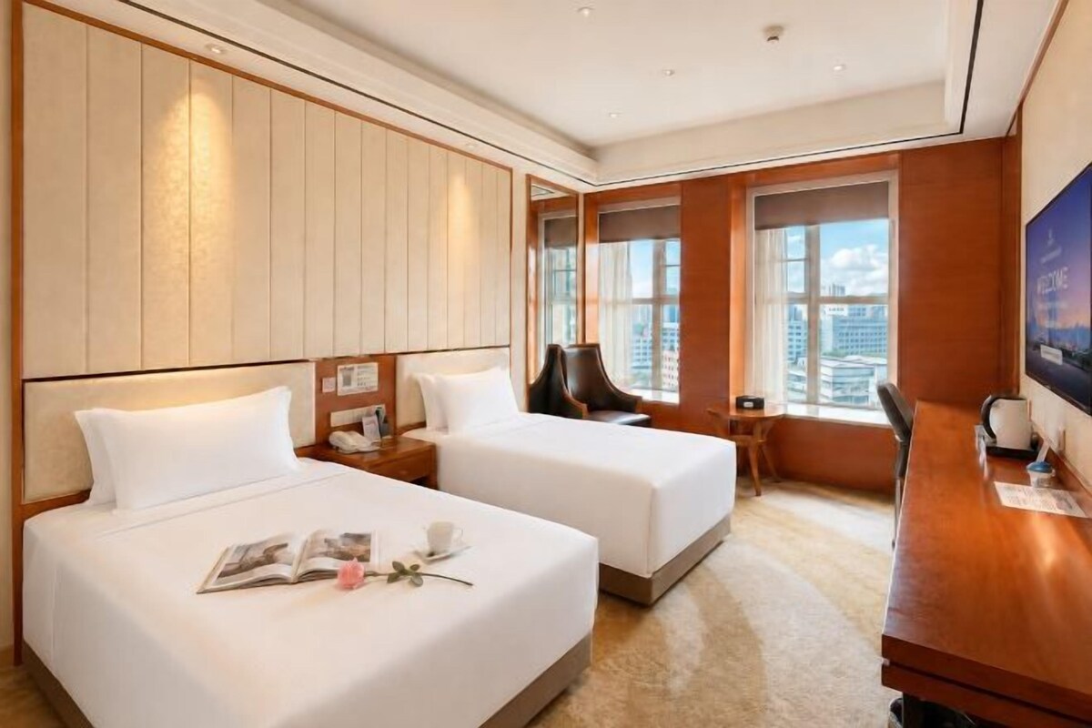 A hotel room with two beds, a desk, and a view of the city.