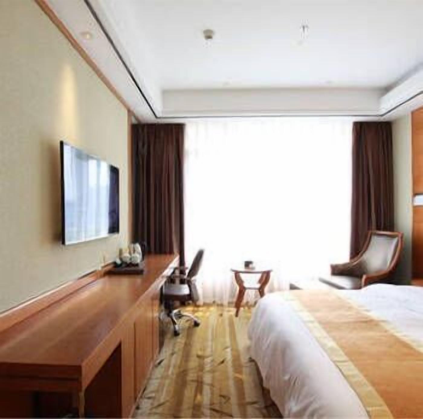 Una habitación de hotel con cama, escritorio, silla, mesita y televisor en la pared.