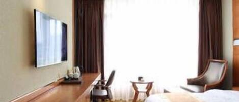 Una habitación de hotel con cama, escritorio, silla, mesita y televisor en la pared.