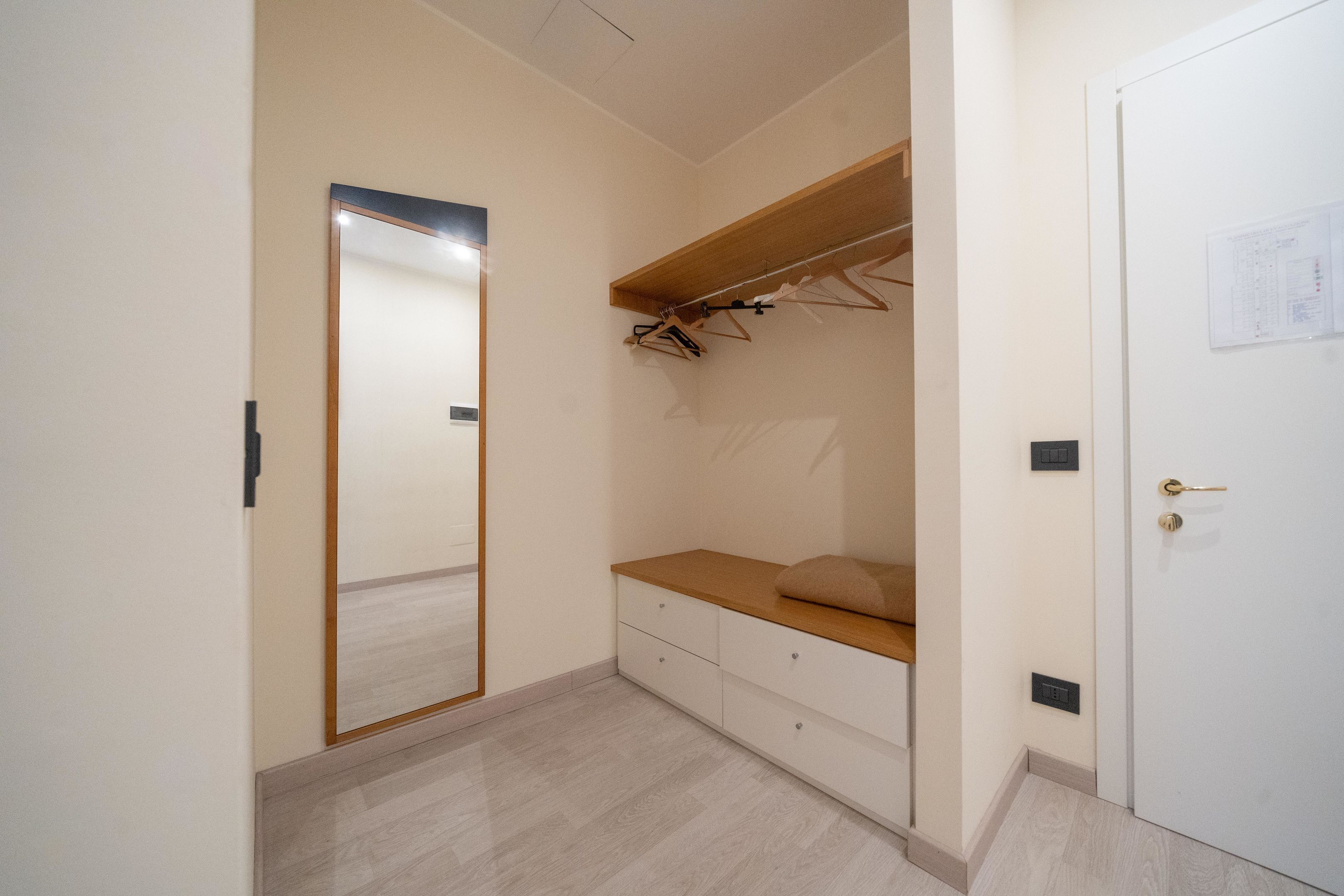 Un dormitorio con un banco de madera, un espejo y una puerta blanca.