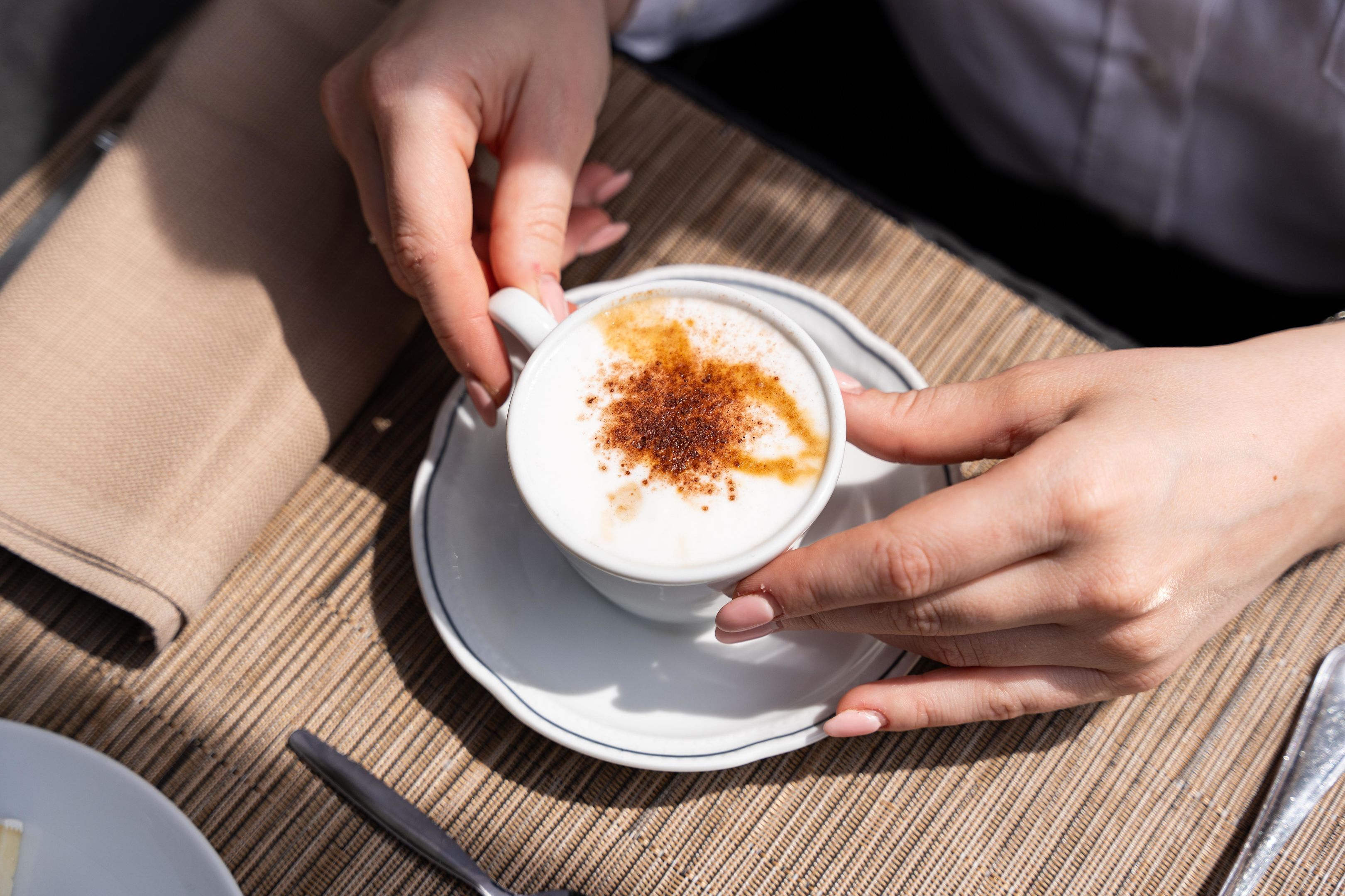 A person holding a cup of coffee with a saucer on a table.