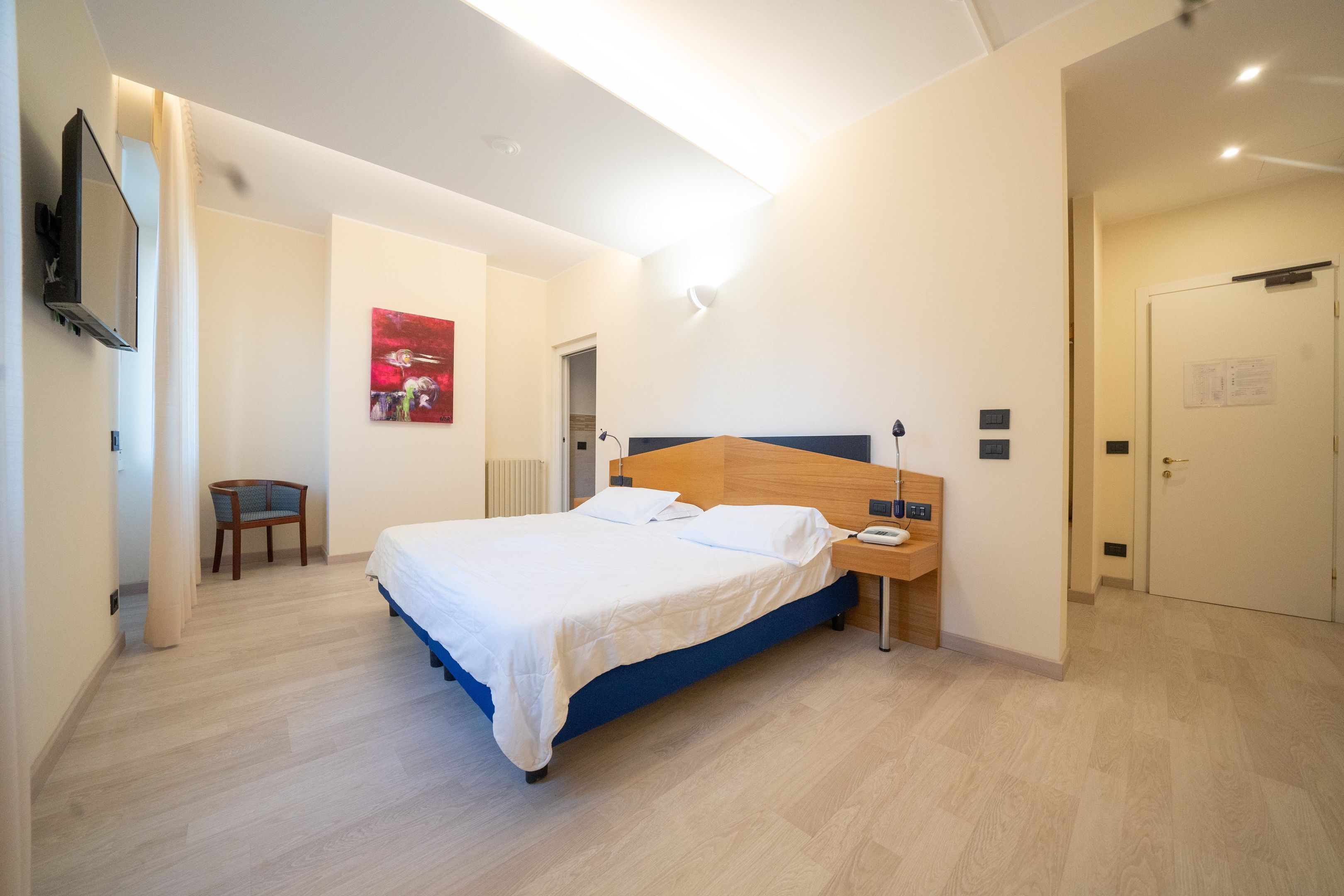 A modern hotel room with a large bed, bedside table, and a flat-screen TV mounted on the wall.
