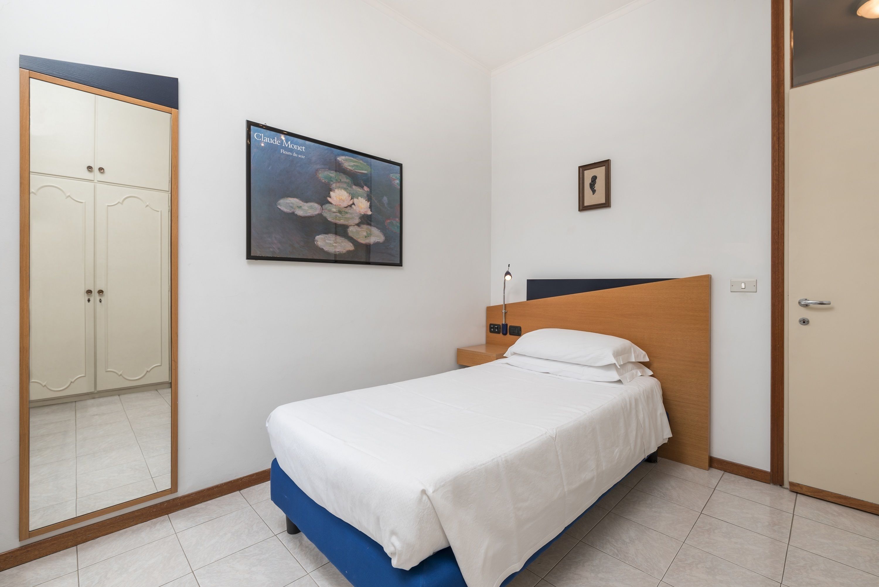 Quarto com uma cama, guarda-roupa, um quadro emoldurado e um cartaz na parede.