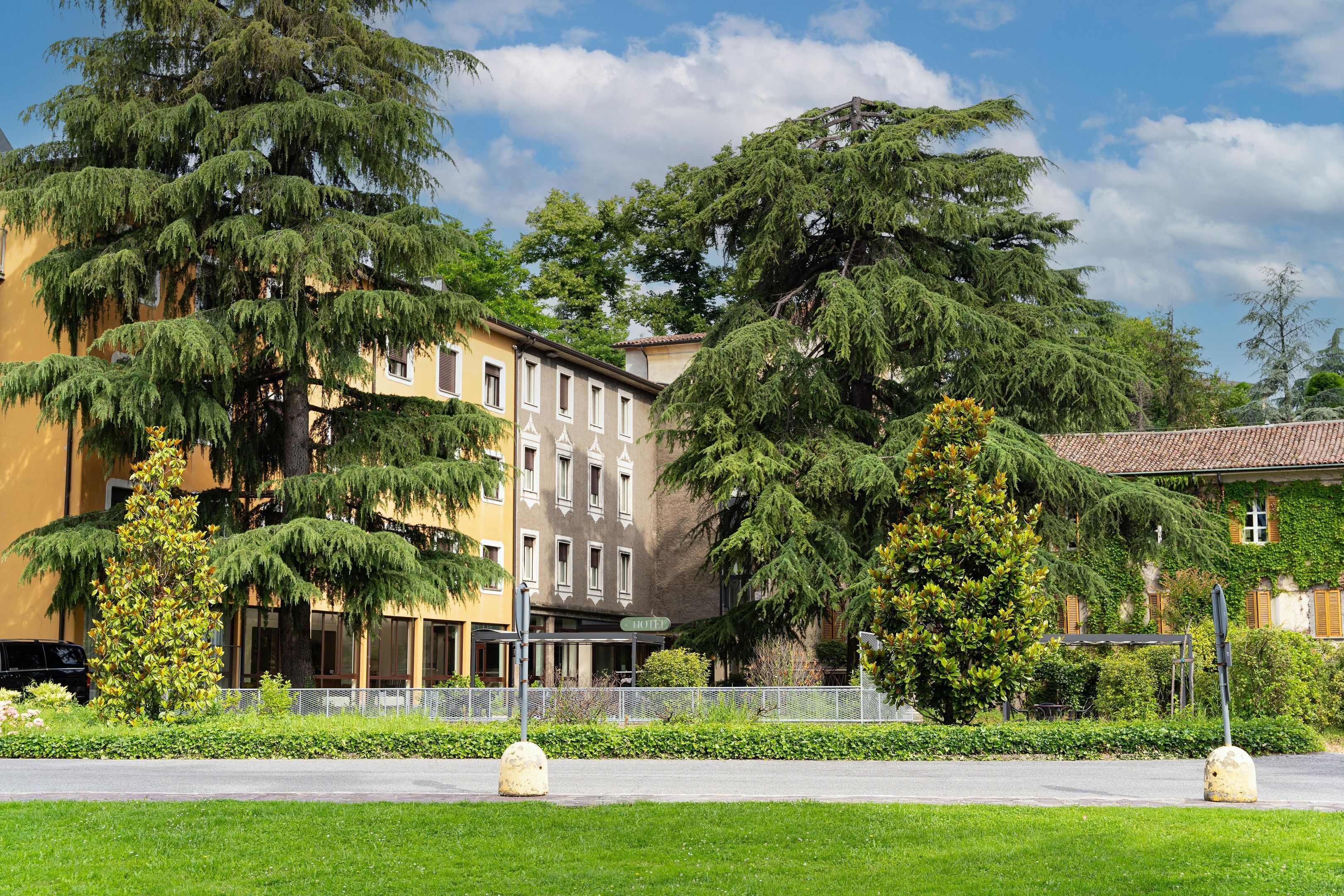 Ein Hotel mit mehreren Etagen, großen Fenstern und einem gepflegten Garten.