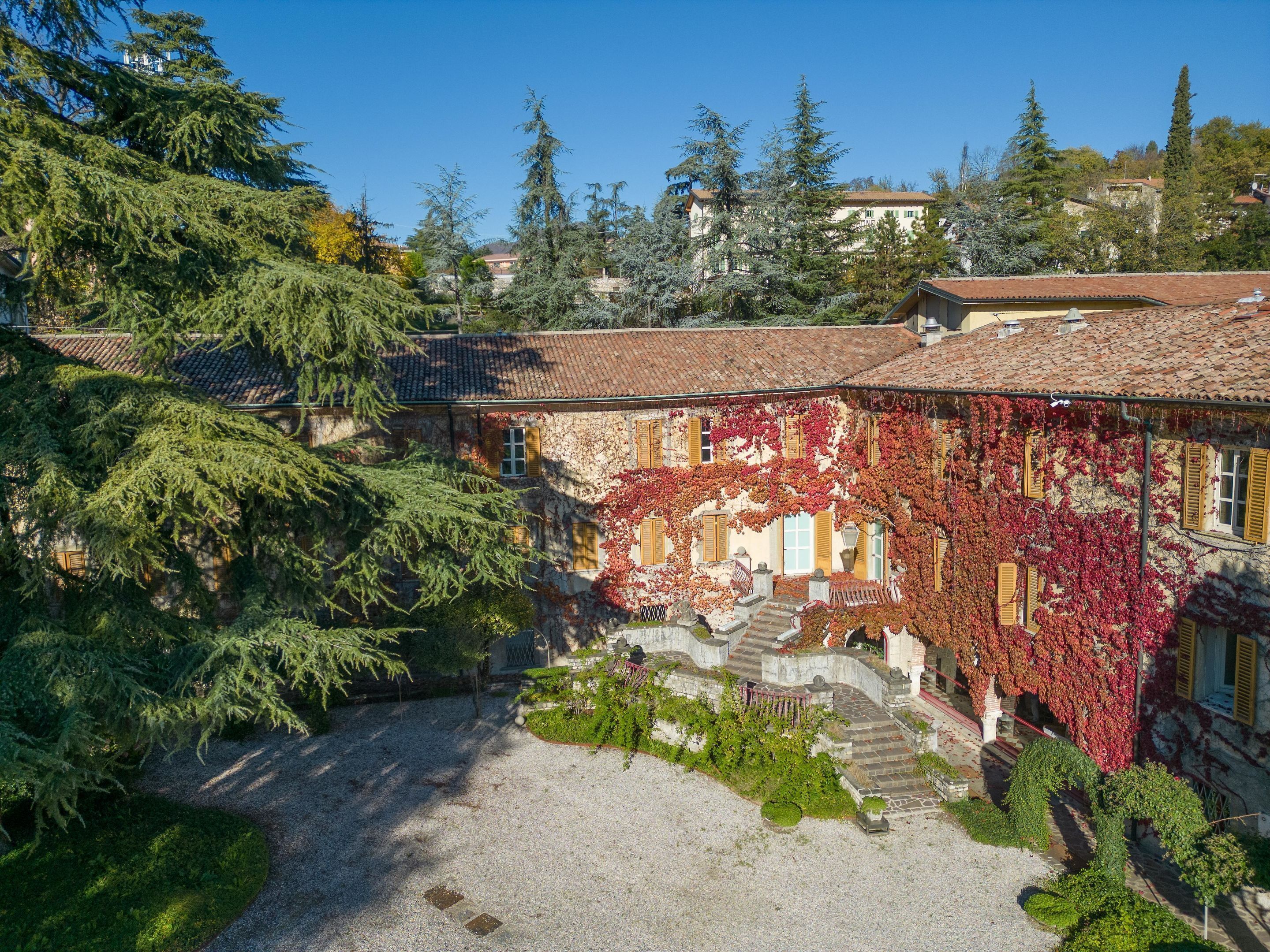 A courtyard with a stone pathway, a small garden, and buildings with red ivy and traditional architecture.
