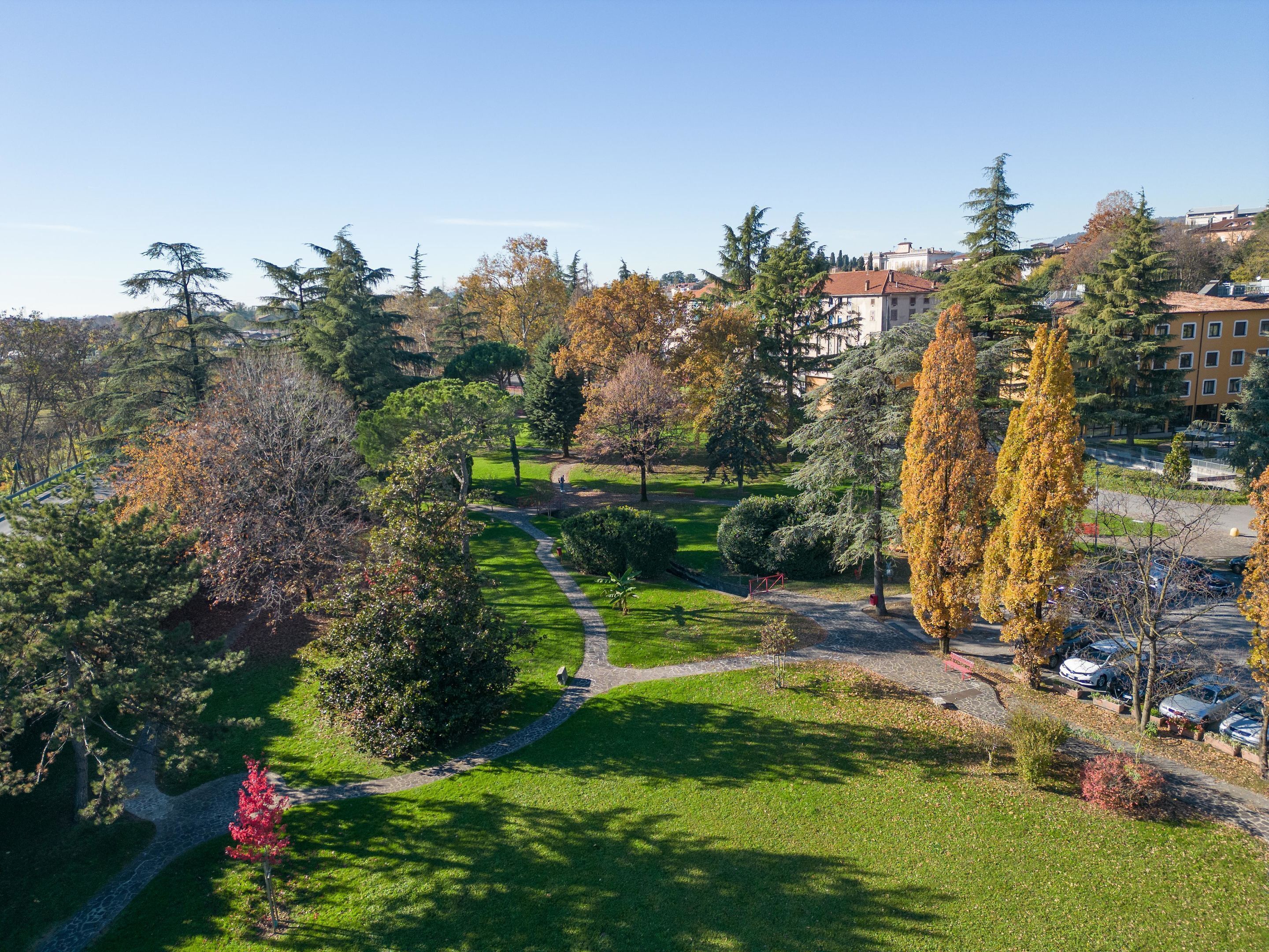 Un parc avec un sentier dallé, de l’herbe verte et des arbres aux feuilles d’automne.