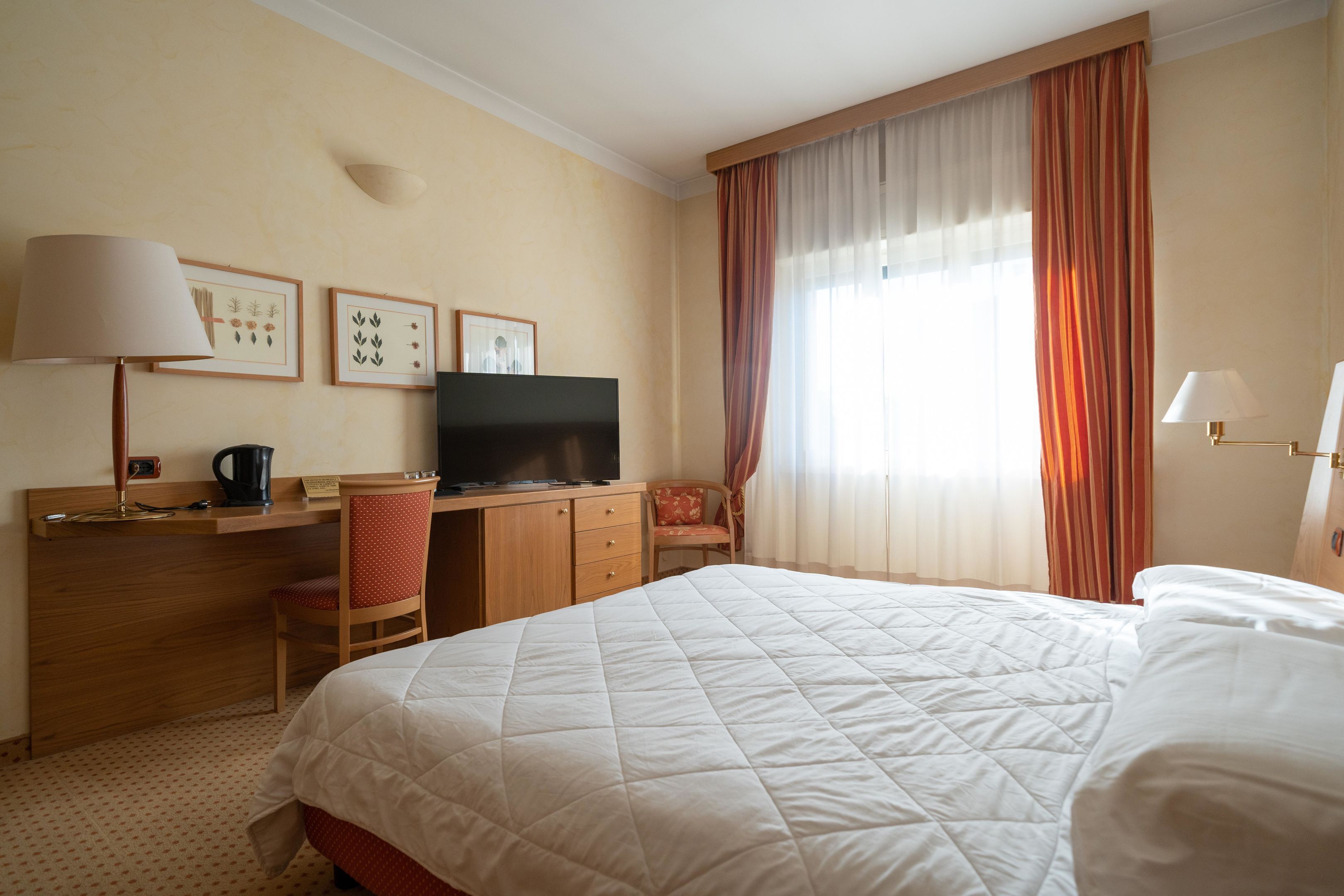 Een hotelkamer met een bed, een bureau met een televisie, een stoel en een raam met gordijnen.