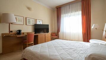 Een hotelkamer met een bed, een bureau met een televisie, een stoel en een raam met gordijnen.