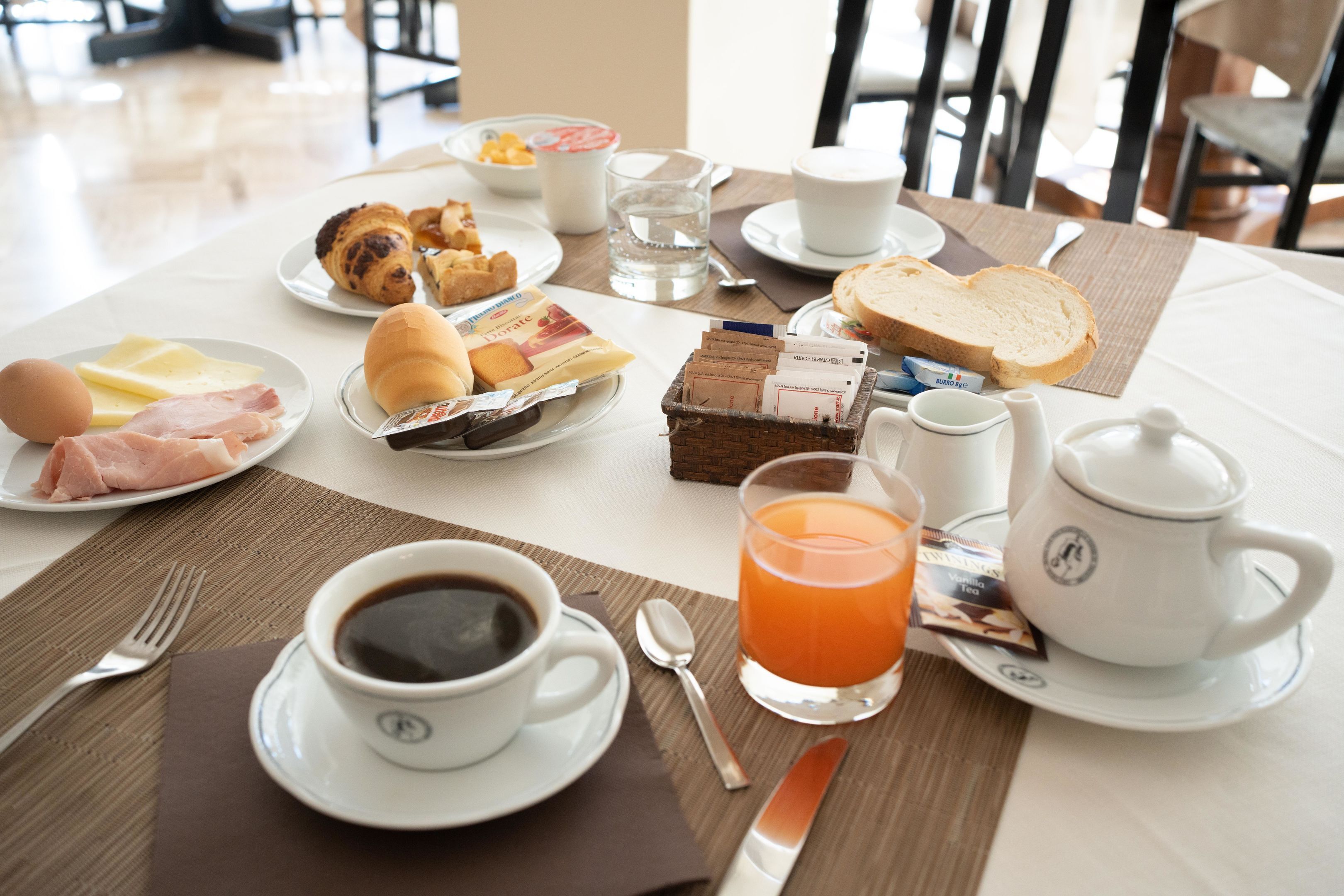 Una mesa de desayuno con croissants, pasteles, huevos, jamón, queso, jugo, café y té.
