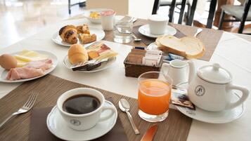 Una mesa de desayuno con croissants, pasteles, huevos, jamón, queso, jugo, café y té.