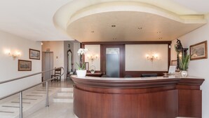 A reception area with a curved wooden desk, a staircase with metal railings, and a potted orchid. - Hotel San Pancrazio (Trescore Balneario)
