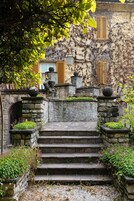 Una scala in pietra conduce a un edificio con persiane di legno, immerso nel verde e ornato da elementi decorativi in pietra.