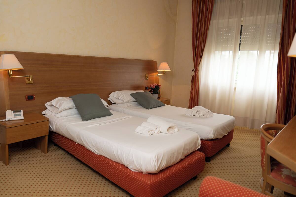 Une chambre d’hôtel avec deux lits, une tête de lit en bois, une table de chevet avec un téléphone et un bureau avec une chaise.