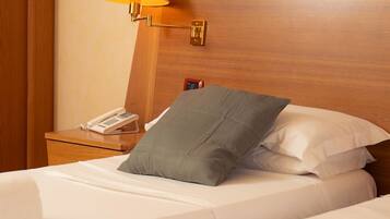 A hotel room with a wooden headboard, a bedside lamp, a telephone, and a bed with white bedding and a grey pillow.