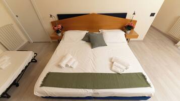 Una cama bien hecha con sábanas blancas, un edredón verde y dos almohadas. Hay dos mesitas de noche con lámparas y arreglos florales.