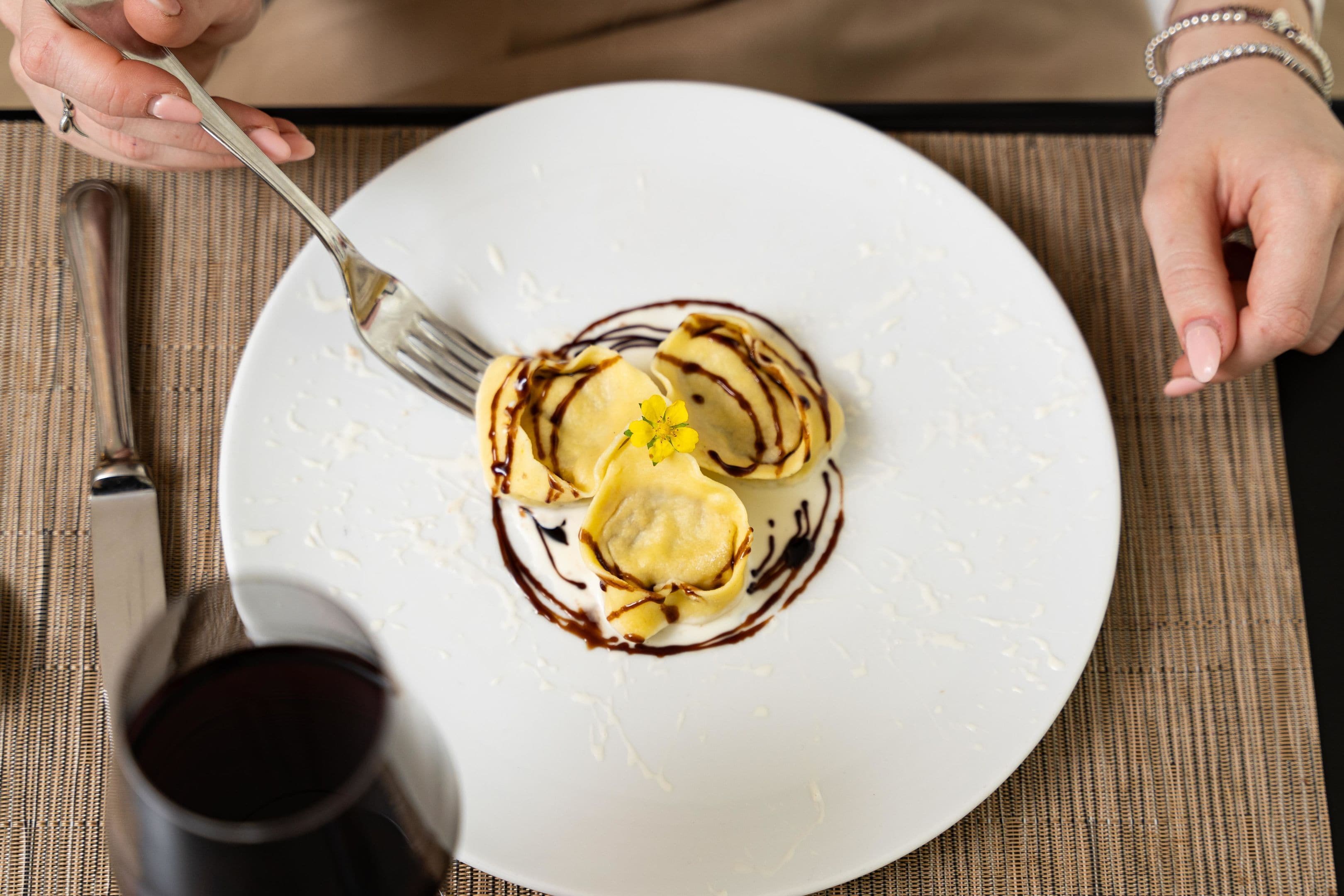A white plate with a dessert, a fork, and a glass of red wine on a table.