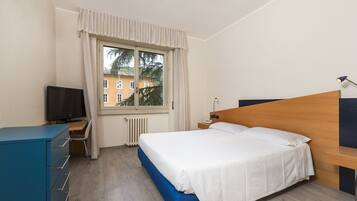 Habitación de hotel con cama, escritorio con televisor, cómoda y ventana con cortinas.