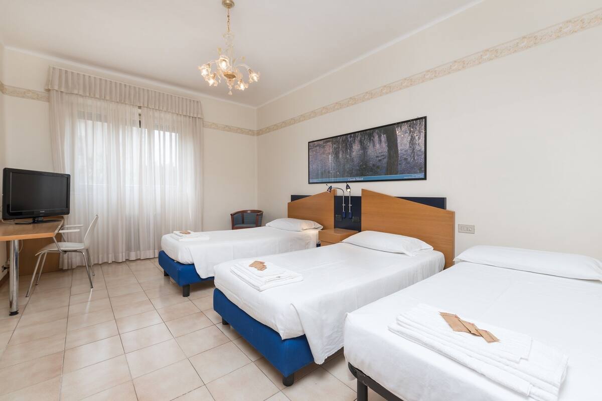 Une chambre d’hôtel avec trois lits, un bureau avec un ordinateur et une télévision.